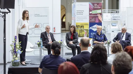 Frau steht auf einer Bühne vor einer Menschenmenge und hält einen Vortrag über Familienunternehmen in Ostdeutschland